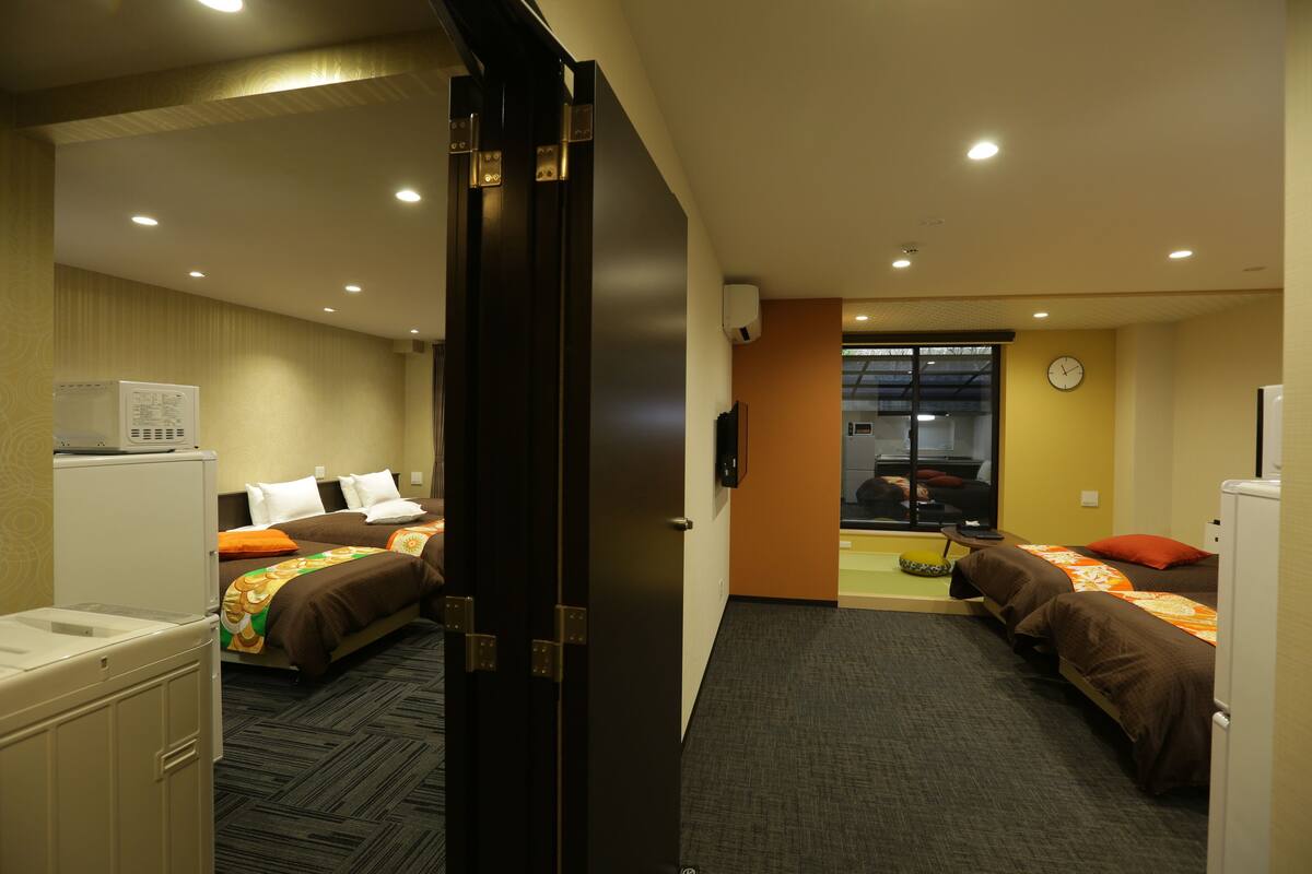 Habitación de hotel con dos camas, un escritorio, una silla, una mesita, un refrigerador y una ventana.