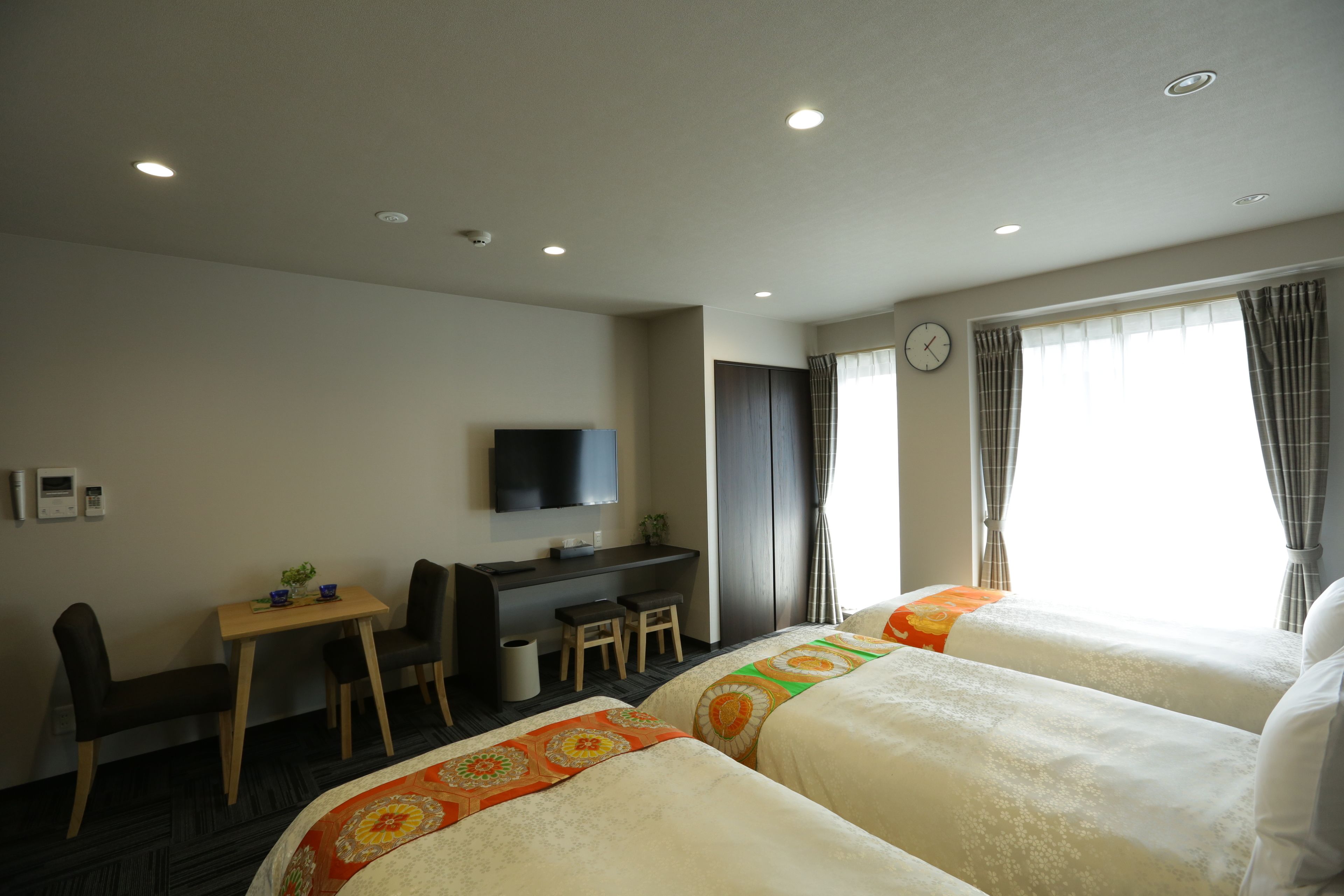 A hotel room with two beds, a desk, a chair, a TV, and a window with curtains.