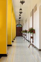 A hallway with yellow walls, patterned floor tiles, and wooden doors with flower arrangements.