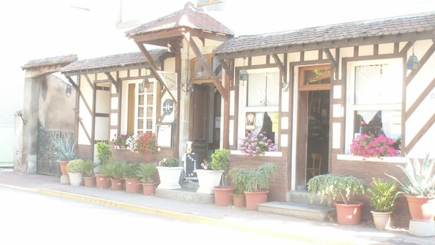 Een gebouw met een traditionele architectuur, een houten gevel en meerdere ramen. Er staan potplanten langs de voorkant, en een bord dat een restaurant of café aangeeft.