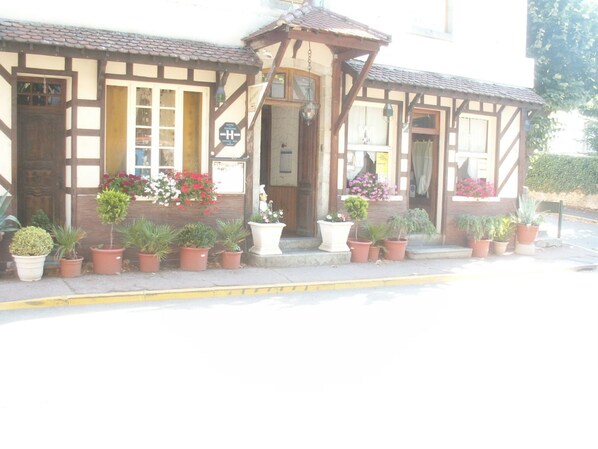 Un edificio tradicional con un cartel que indica que es un hotel. Hay varias plantas en macetas frente a la entrada.