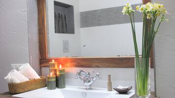 Un baño con lavamanos, espejo, velas y un florero con flores.