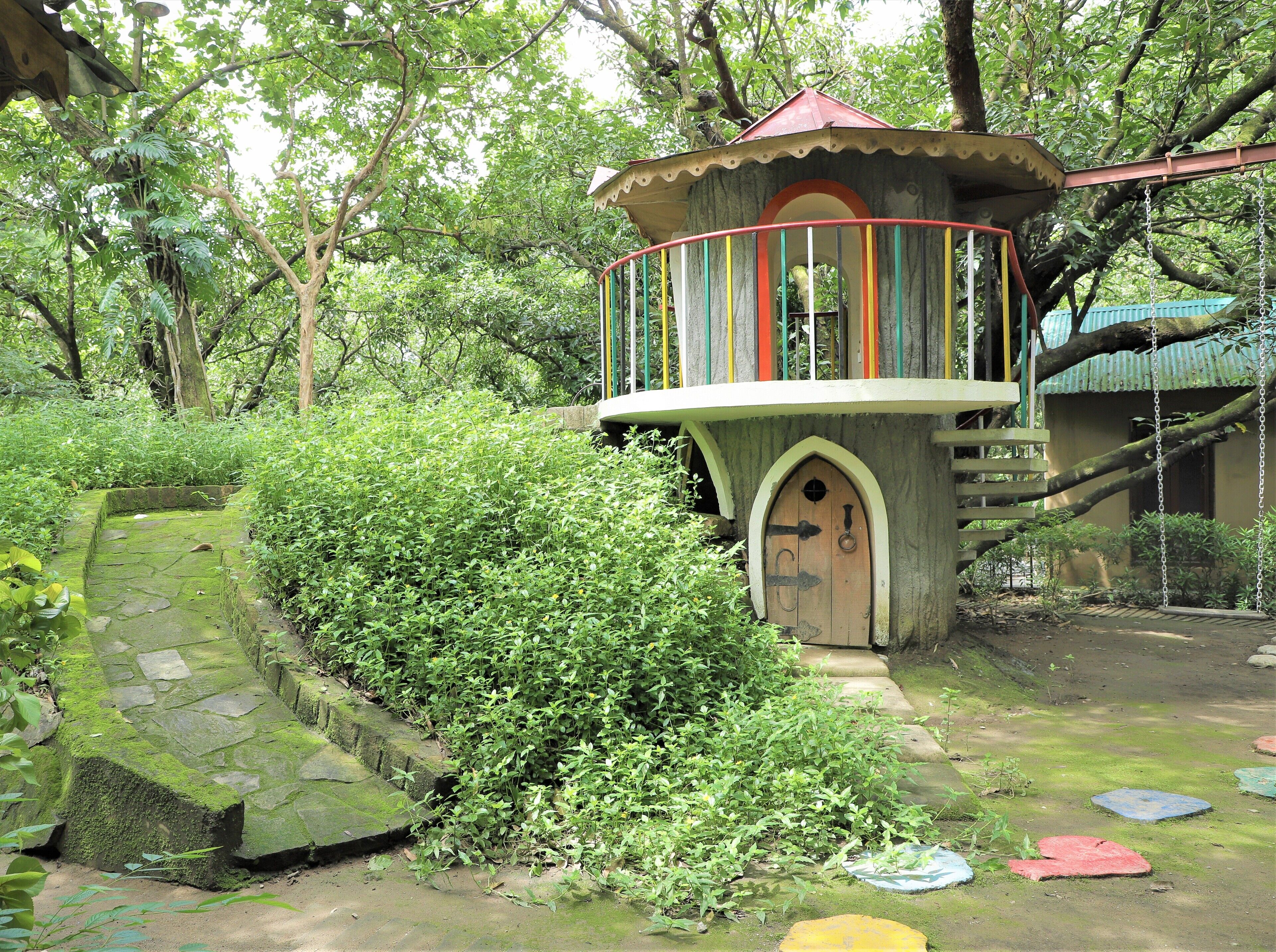 A small, rustic treehouse with a wooden door and a balcony with colorful railings.