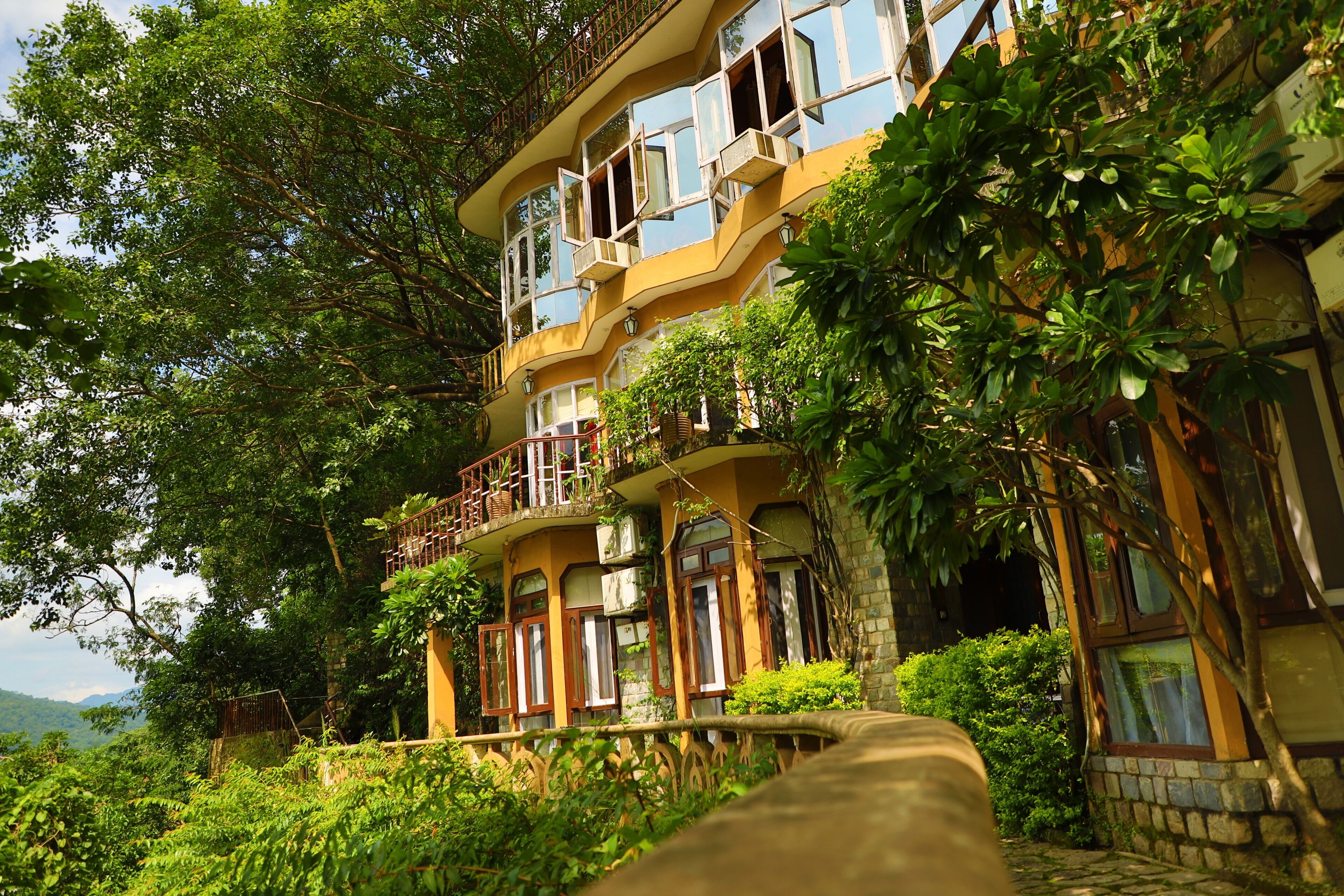 A multi-story building with balconies, surrounded by lush greenery.