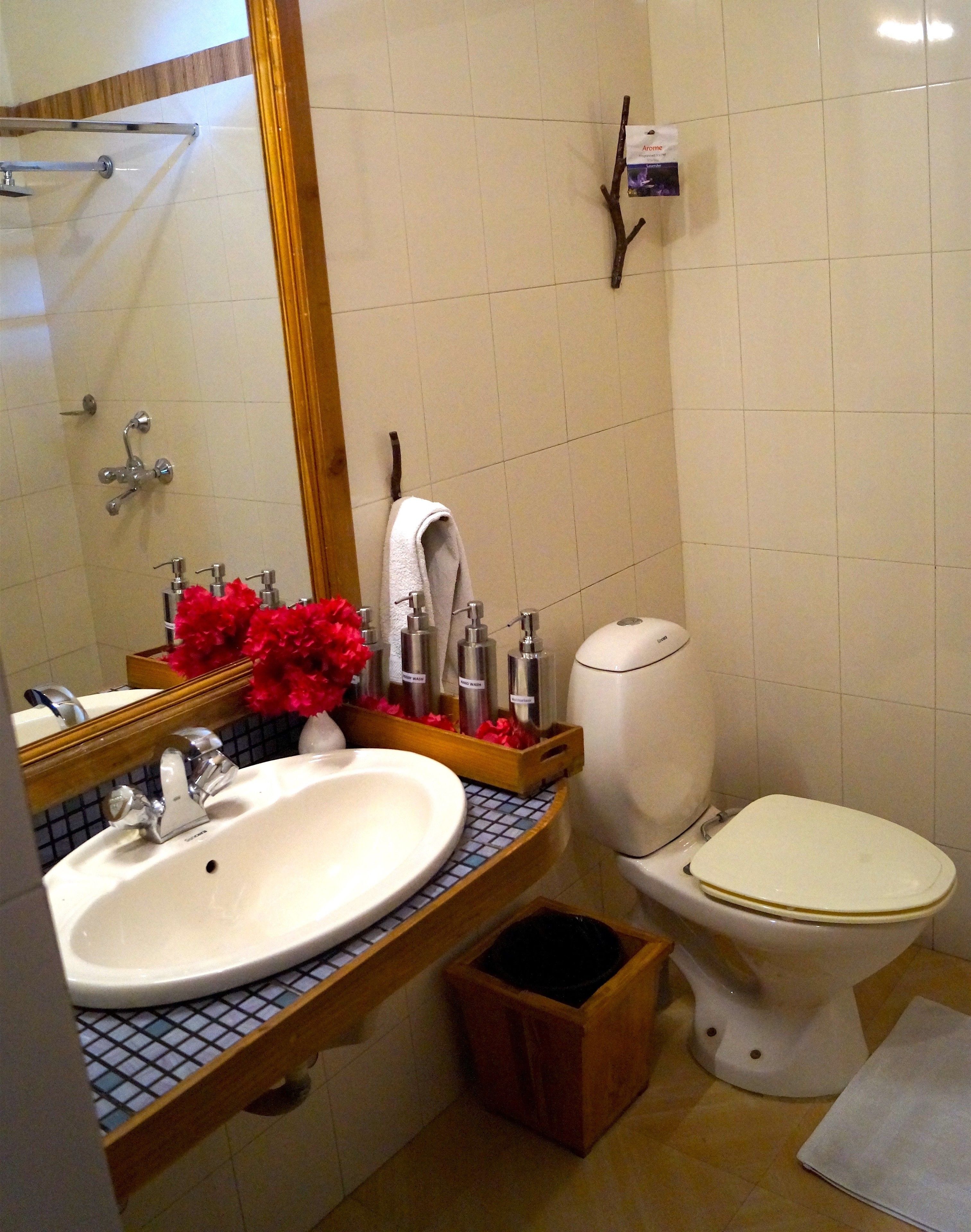 A bathroom with a white sink, mirror, and toilet. There are toiletries on the sink counter and a small trash bin.