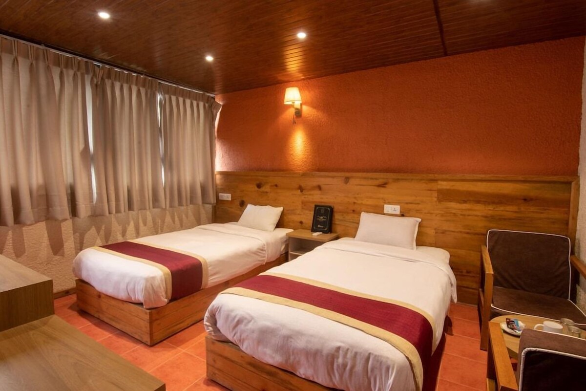 A hotel room with two beds, wooden headboard, a nightstand, a chair, and a table.