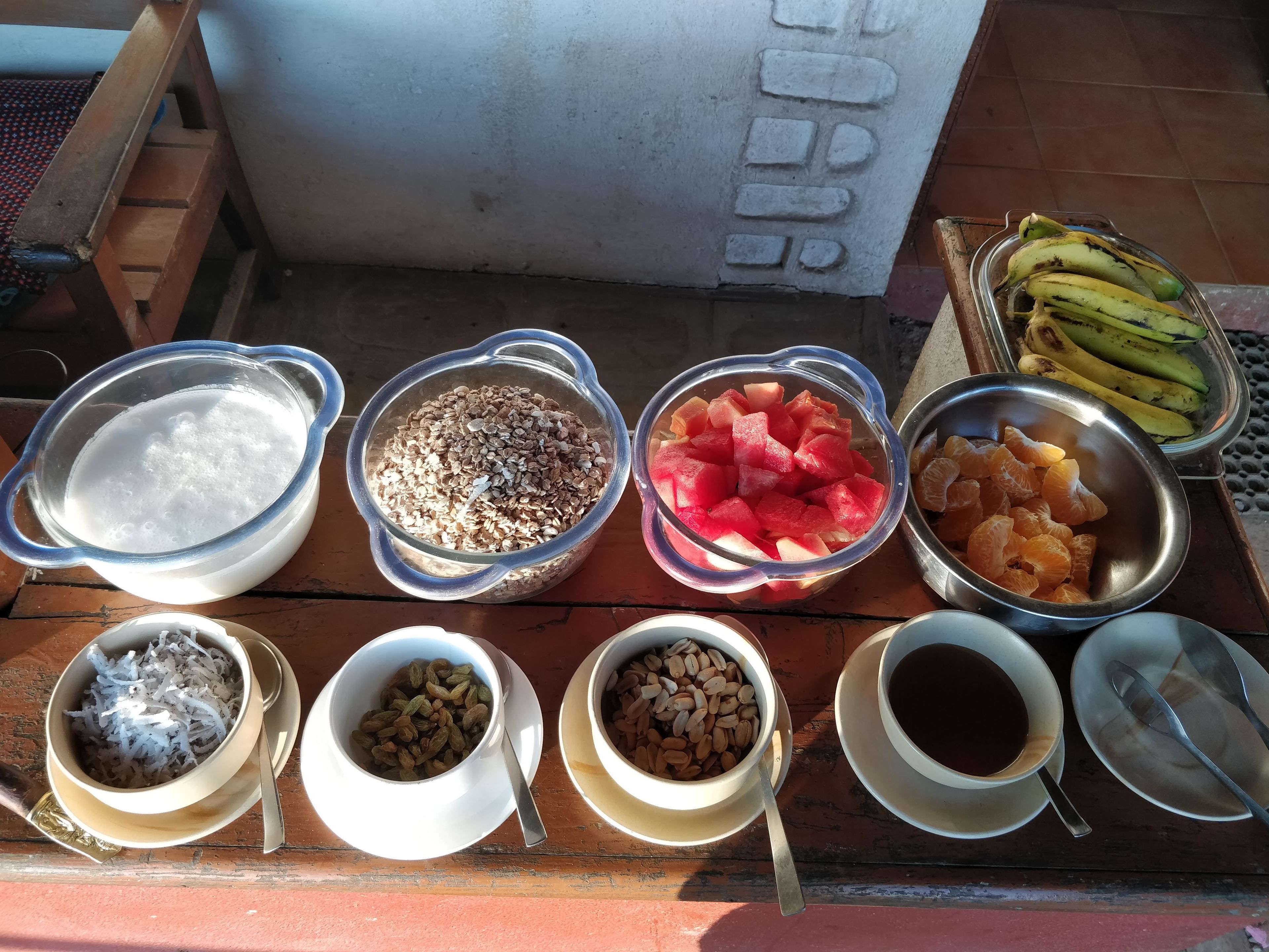 A table with various food items including bowls of rice, watermelon, oranges, and bananas.