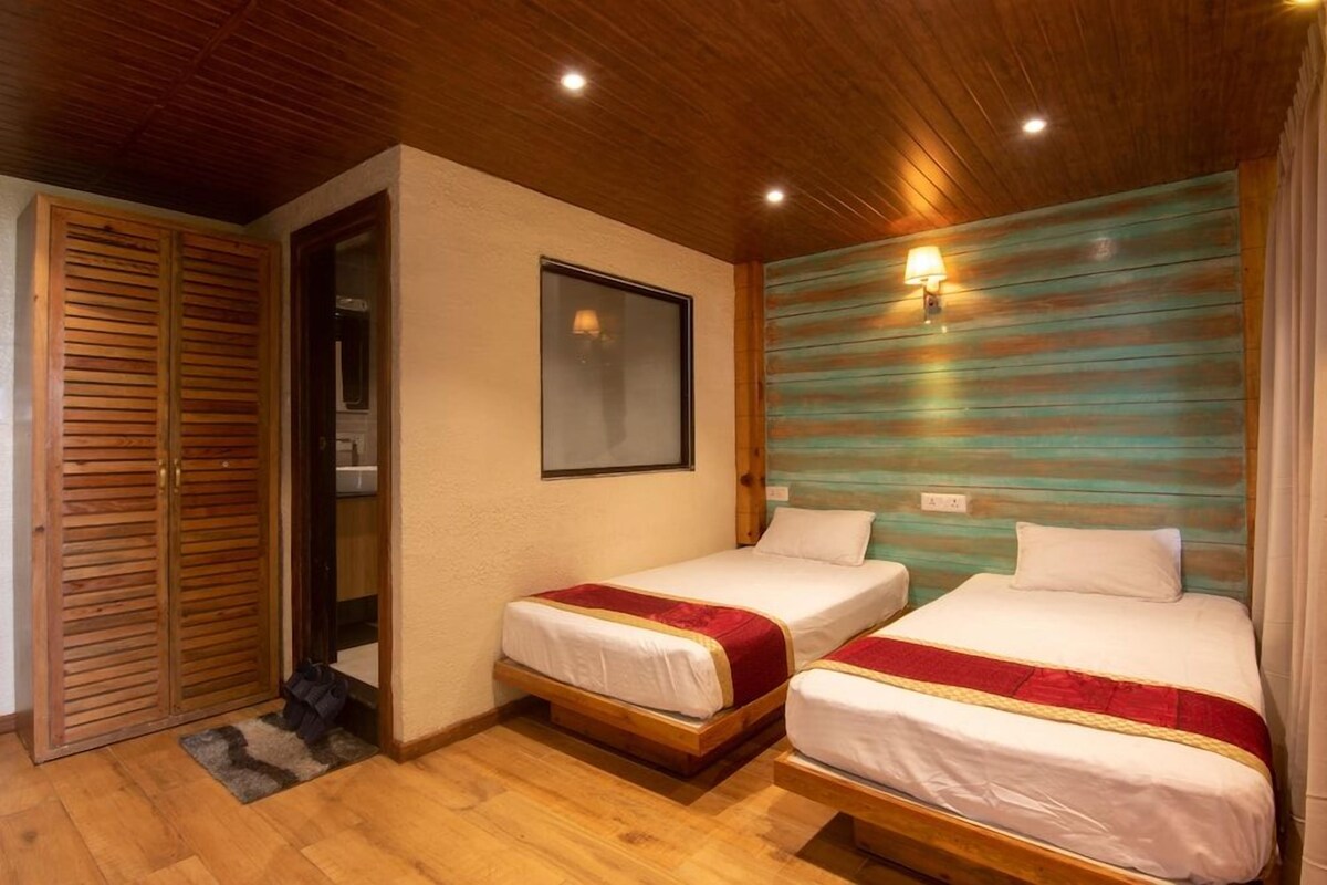 A room with two beds, wooden flooring, a wooden ceiling, a wooden wardrobe, a mirror, and a wall-mounted light fixture.