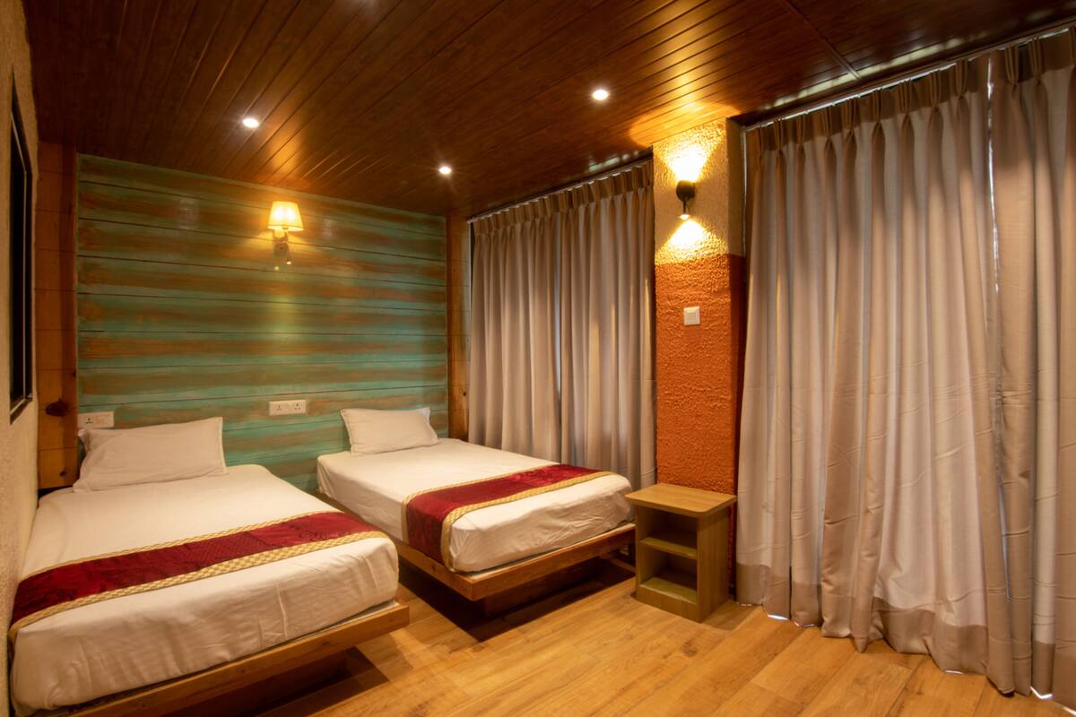 Una habitación con dos camas, suelo de madera, pared de ladrillo y una ventana con cortinas.
