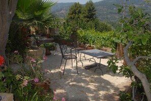 A garden patio with a table and chairs, surrounded by potted plants and flowers.