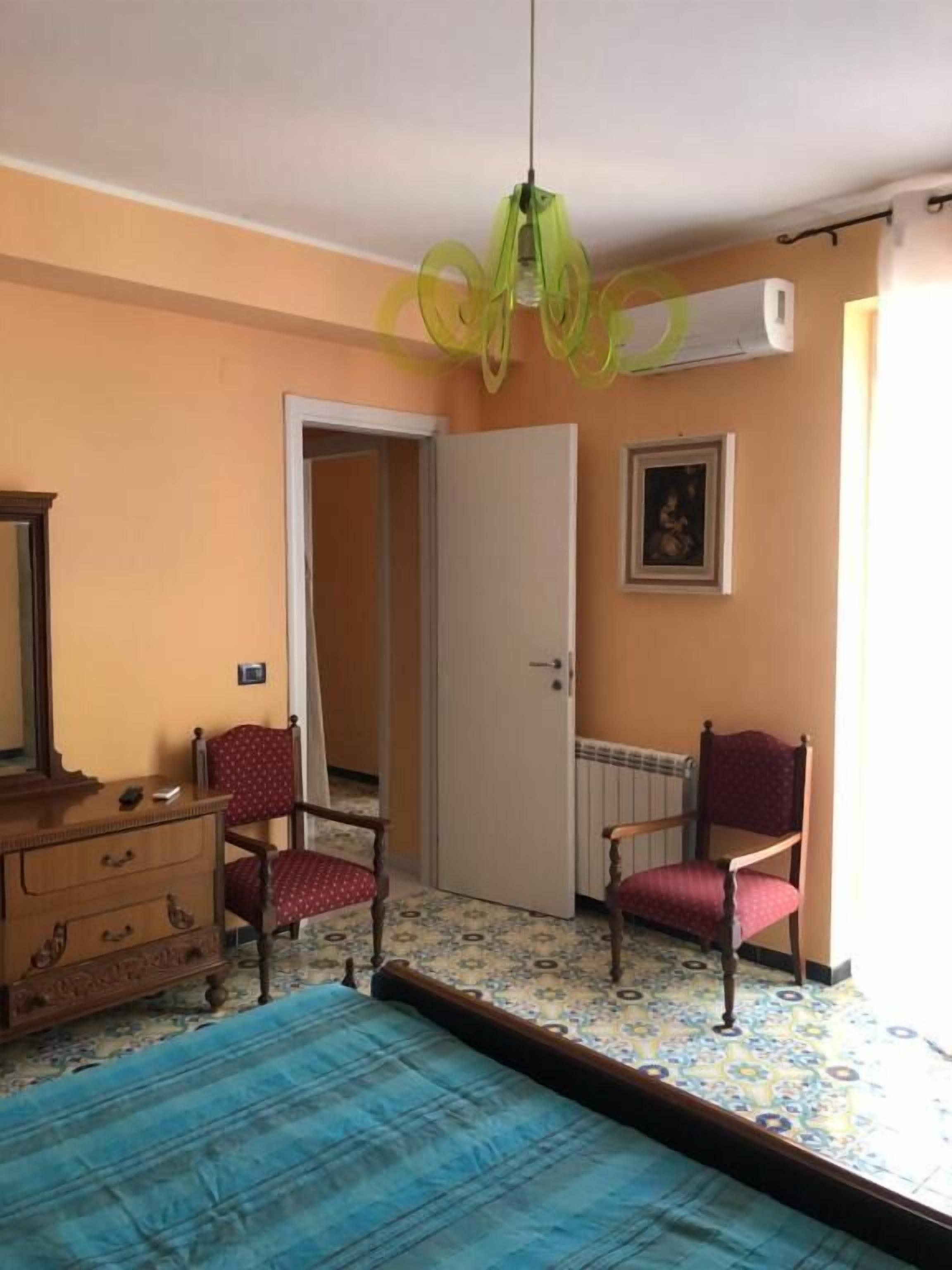 A bedroom with a bed, two chairs, a dresser, and a door leading to another room.
