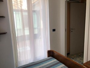 A room with a bed, a door, and a window with sheer curtains. - B&B villa zia Febronia (Patti)