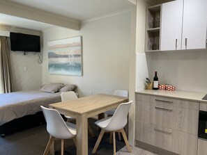 A compact hotel room with a bed, a dining table with chairs, a kitchen area with cabinets, and a mounted TV. - tyrola 4 (Thredbo)
