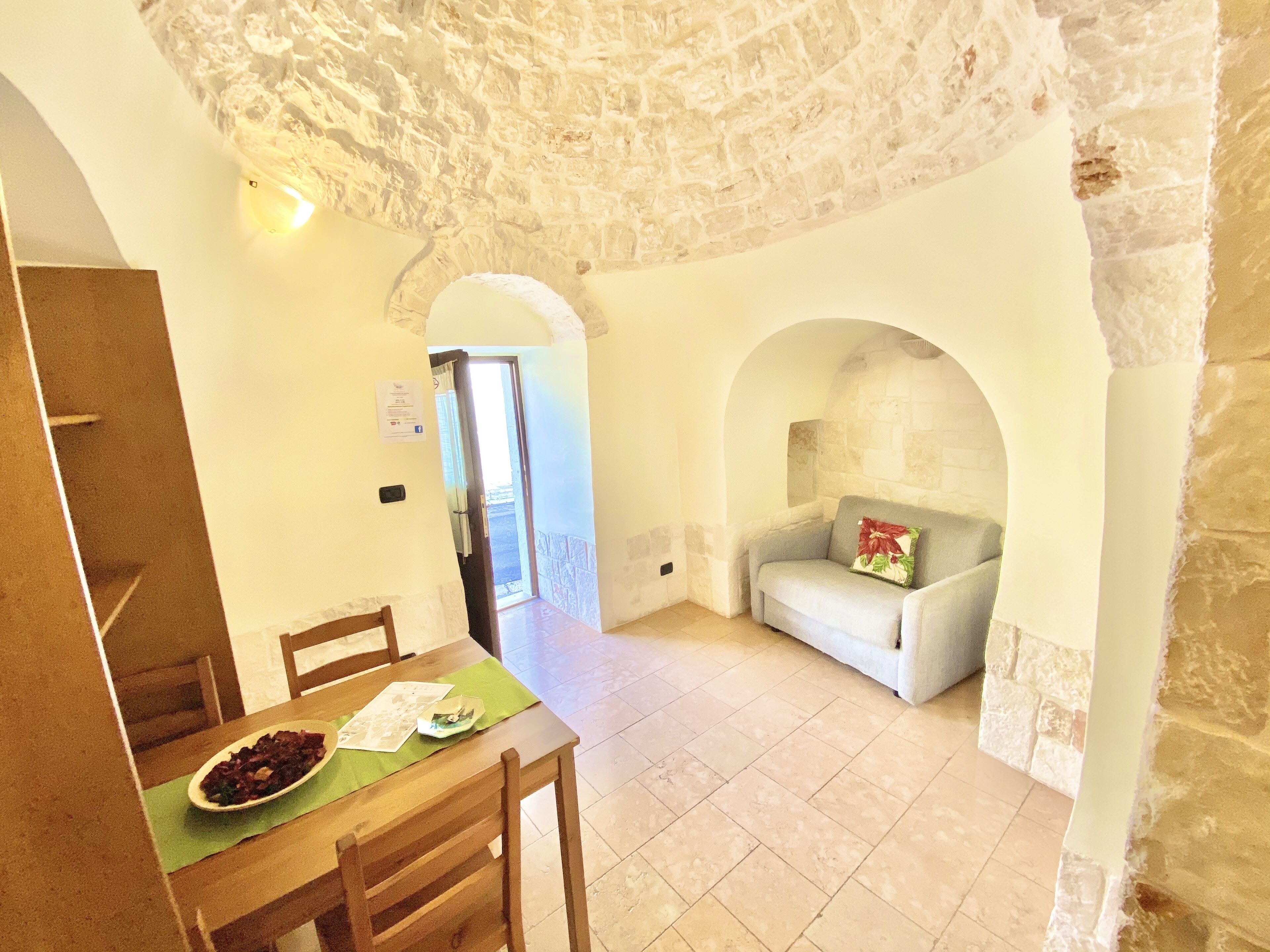 Un coin repas avec une table dressée pour deux personnes, un canapé avec un coussin et un mur en pierre.