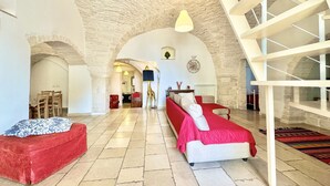 A spacious room with a high arched ceiling, a staircase, and a cozy seating area with a red sofa and a white bed. - Trulli Fenice Alberobello (Alberobello)