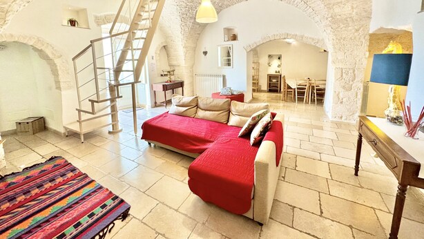A spacious room with a red sofa, a staircase, and a dining area. - Trulli Fenice Alberobello (Alberobello)