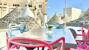 An outdoor seating area with a table and chairs, a stone wall, and a historic building with a bell tower in the background. - Trulli Fenice Alberobello (Alberobello)