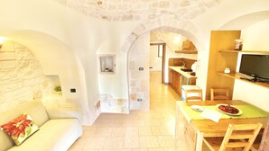 A cozy living area with a stone wall, a wooden dining table, and a sofa. - Trulli Fenice Alberobello (Alberobello)