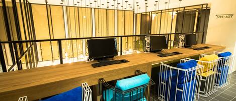A modern reception area with a wooden desk, two computer monitors, and a phone. There are three blue and one yellow cushioned bar stools.