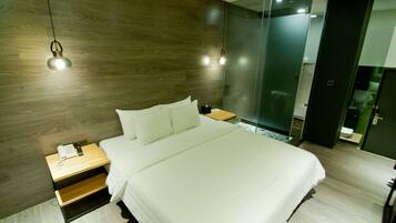 A modern hotel room with a wooden headboard, a large bed with white bedding, a bedside table with a phone and lamp, and a glass partition wall.