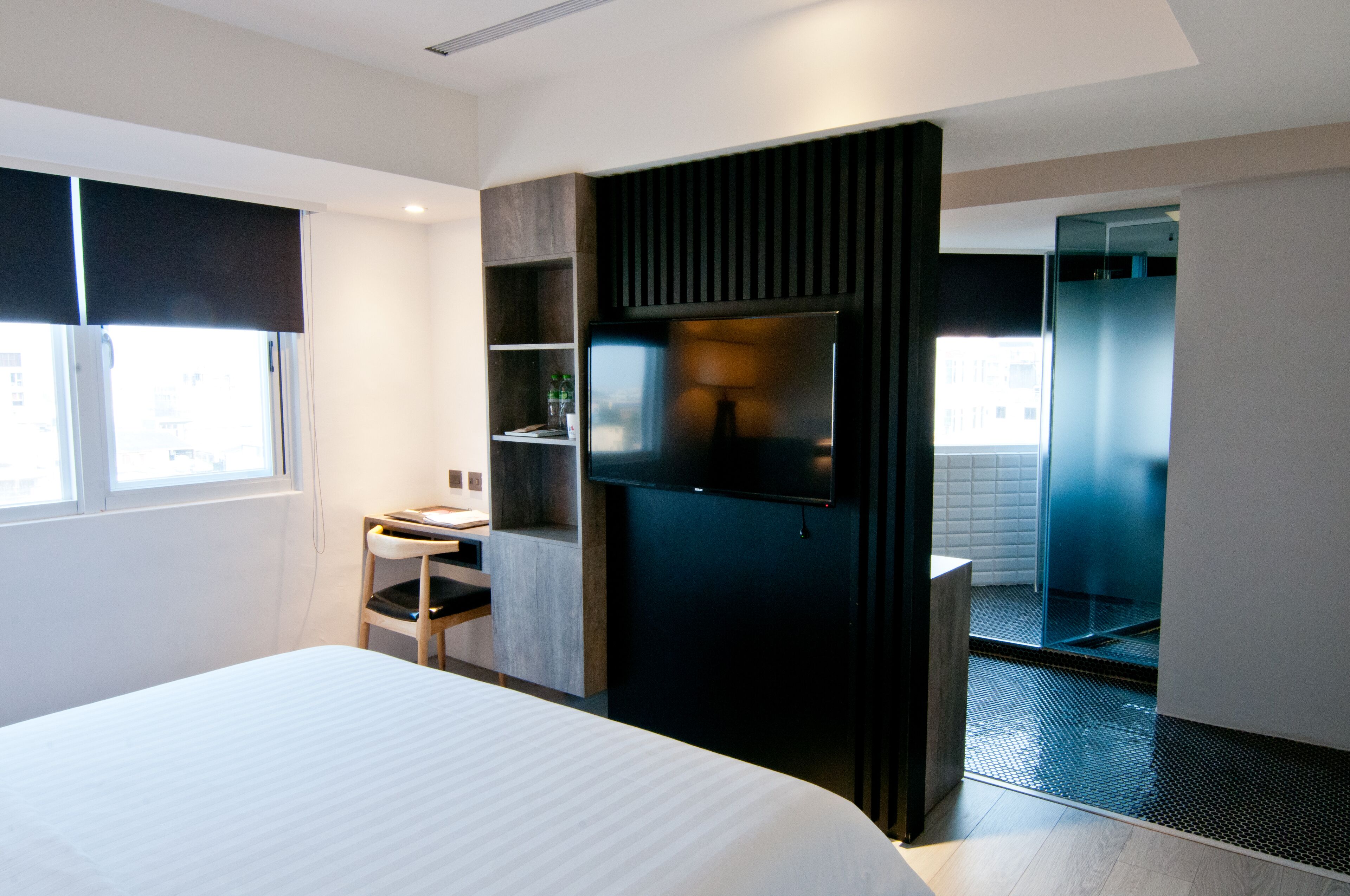 Una camera d'hotel moderna con un letto grande, una scrivania, una TV e un bagno con porta in vetro.