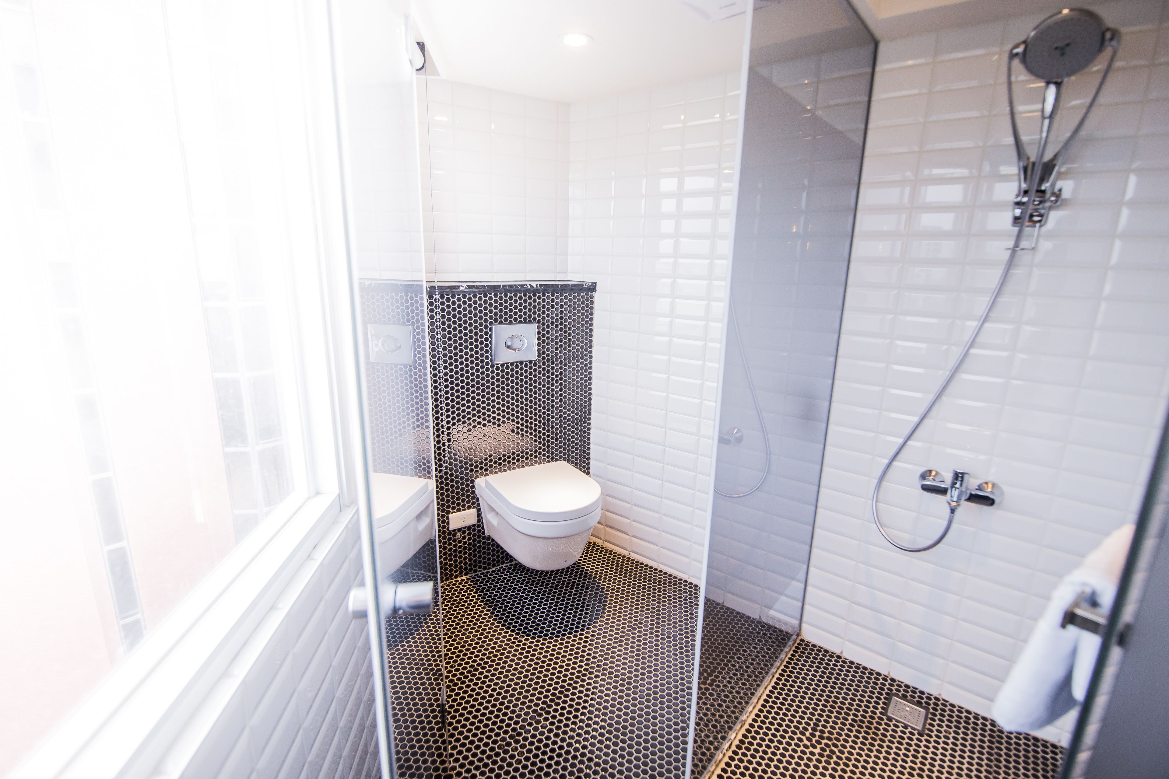 A modern bathroom with a toilet, shower, and a glass partition.
