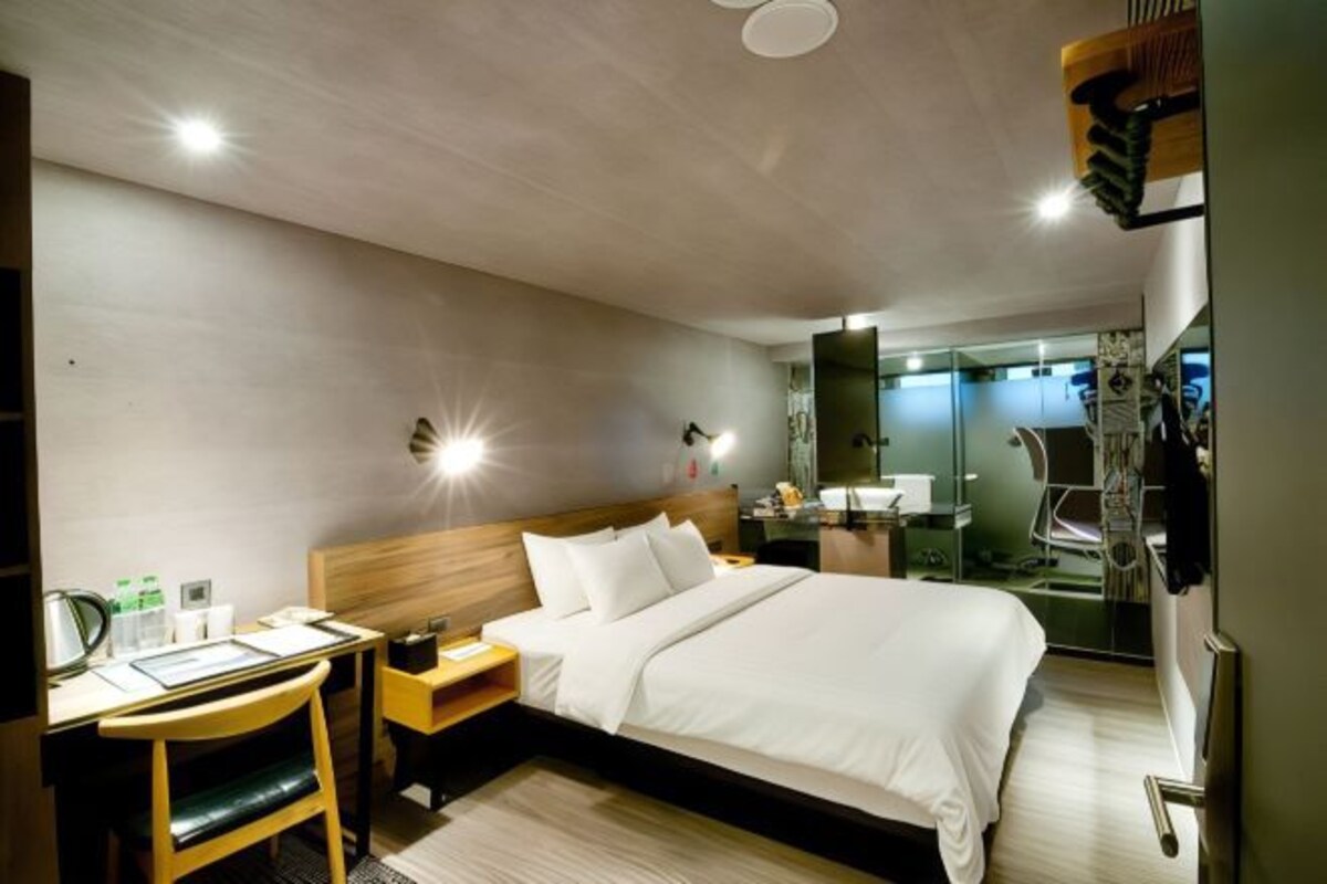 Una habitación de hotel moderna con una cama grande, mesitas de noche, un escritorio y un espejo.