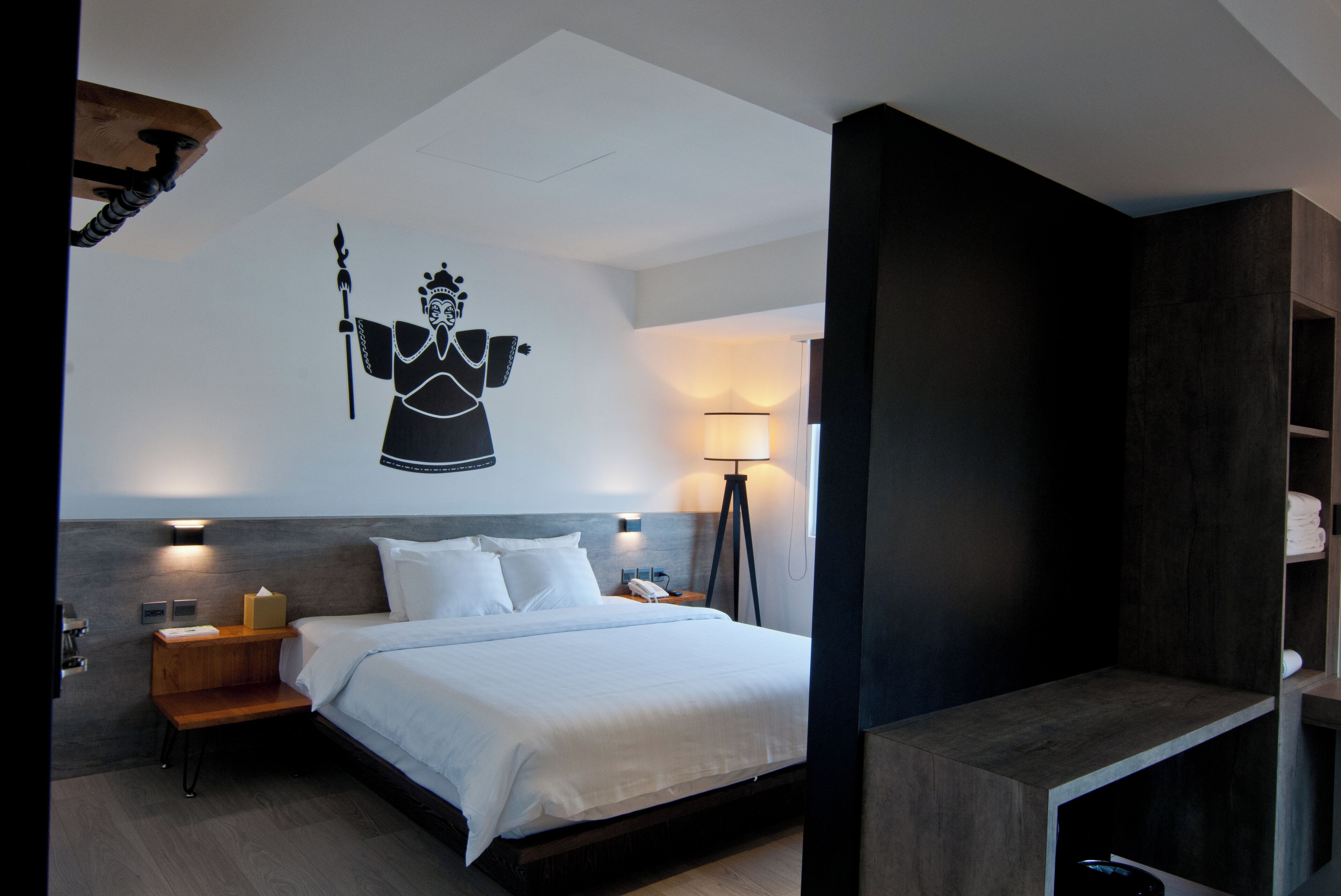 A modern hotel room with a large bed, bedside tables, a wall-mounted artwork, and a floor lamp.