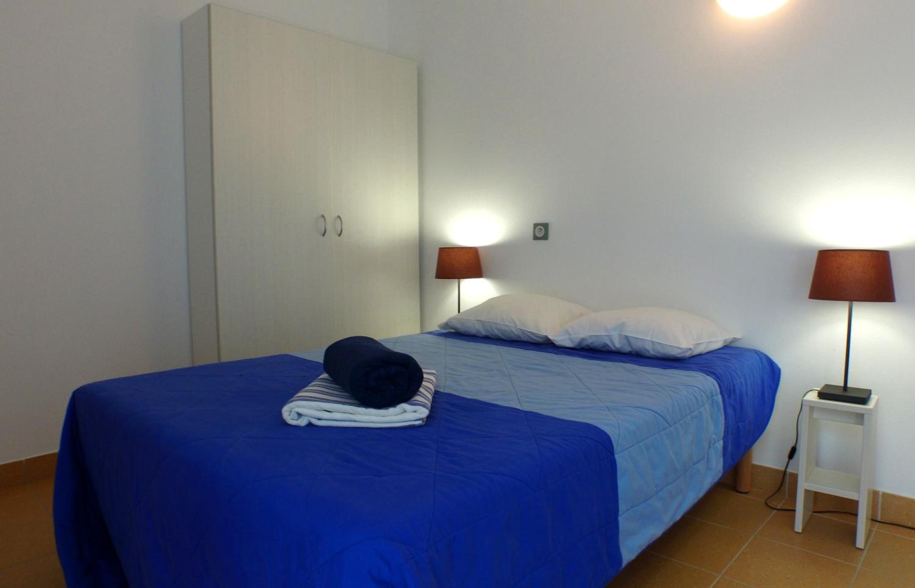 Een hotelkamer met een bed, een kledingkast, twee bedlampen en een kleine tafel.