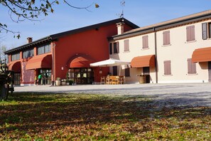 A building with a red facade and a beige section, featuring outdoor seating and a covered area. - Agriturismo Ronchetrin (Gazzo Veronese)