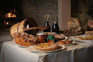 A table with various baked goods, including a basket of bread, a pie, and pastries, with bottles and jars of preserves in the background. - Agriturismo Ronchetrin (Gazzo Veronese)