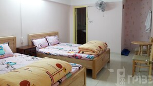 Une chambre avec deux lits, une table de chevet, une chaise, un ventilateur et une porte menant à la salle de bain.