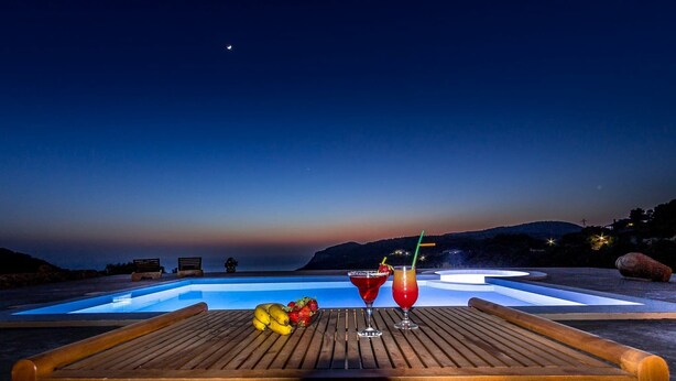 Um deck de madeira com piscina, duas bebidas e frutas.