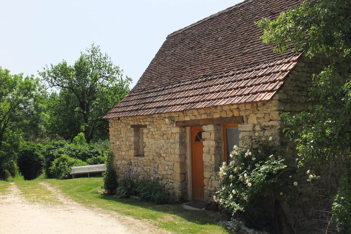 A stone building with a tiled roof, a wooden door, and a small window.