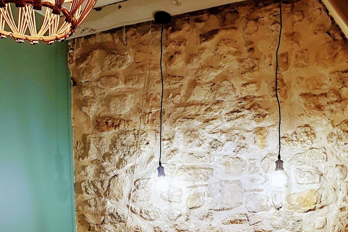 A bedroom with a stone wall, a wooden headboard, and a hanging light fixture.