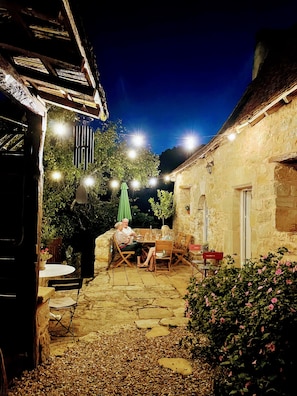 An outdoor patio area with stone flooring, a table with chairs, string lights, and a green umbrella. - Sur le Chemin des Sens (Azerat)