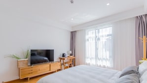 A modern hotel room with a large bed, a wooden dresser with a flat-screen TV, a desk with a chair, and a large window with curtains. - Mishe TEN Boutique Inn (Shanghai)