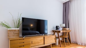 A modern hotel room with a flat-screen TV on a wooden cabinet, a small wooden table with a chair, and a potted plant. - Mishe TEN Boutique Inn (Shanghai)