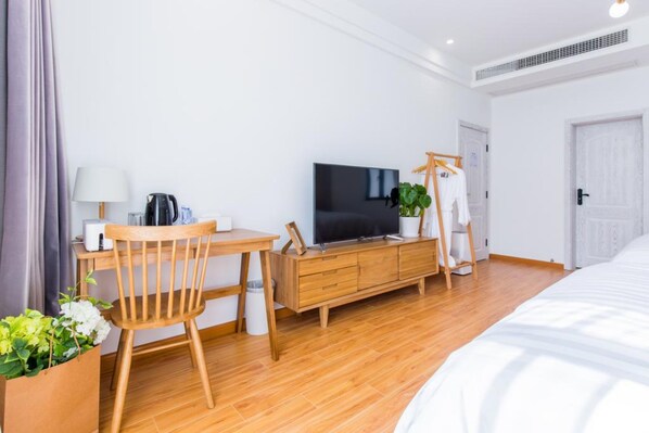 A modern hotel room with a wooden floor, a bed, a TV, a desk with a chair, a wardrobe, and a plant. - Mishe TEN Boutique Inn (Shanghai)