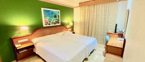 A hotel room with a large bed, a desk with a chair, a painting on the wall, and a window with curtains.