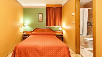 Een hotelkamer met een bed, twee bedlampjes, een nachtkastje, een ingelijste foto aan de muur, en uitzicht op de badkamer door een open deur.