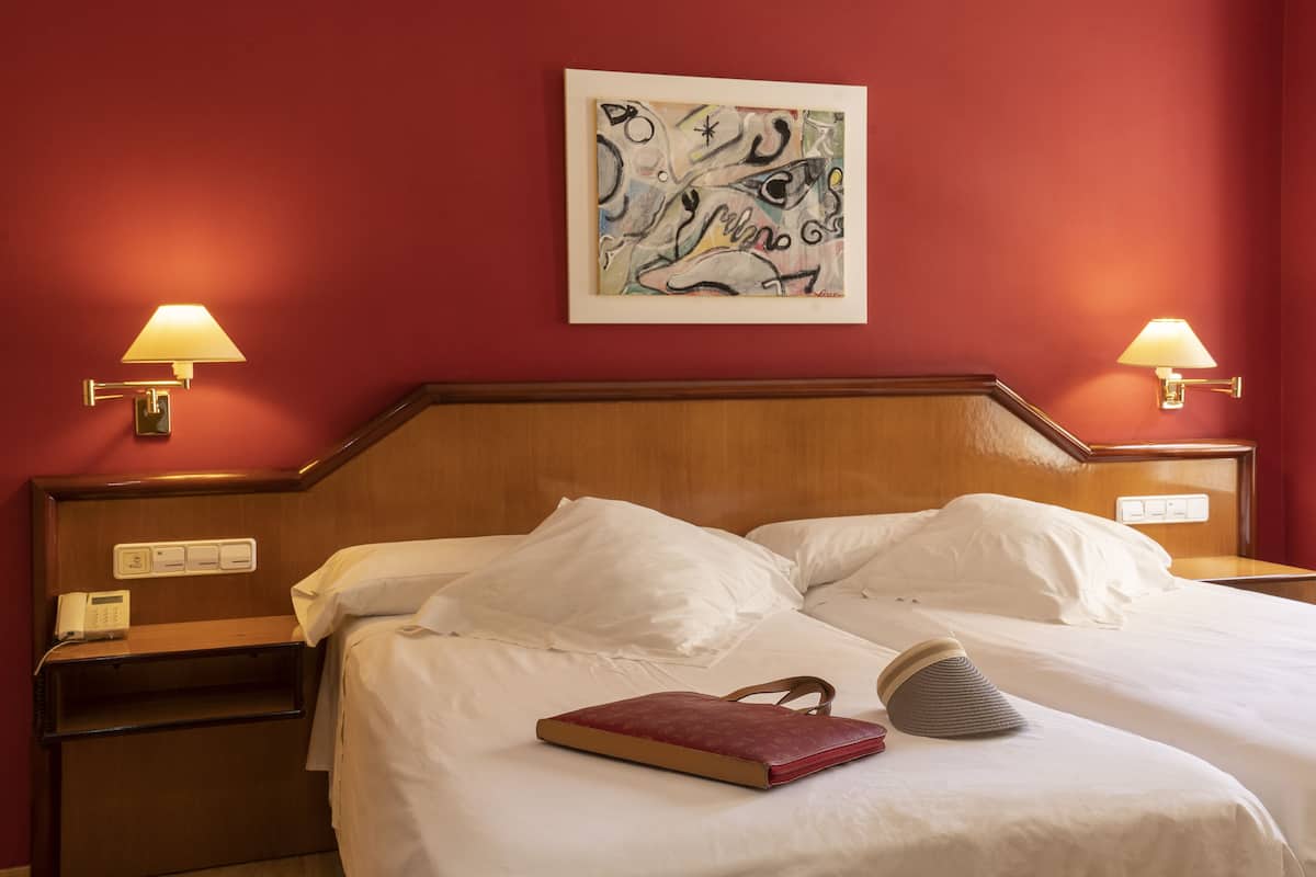 A hotel room with a wooden headboard, white bedding, a red book, and two bedside lamps.