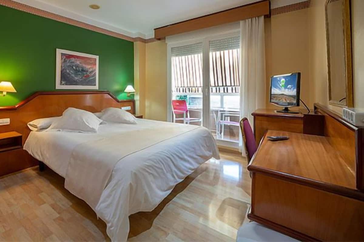 A hotel room with a bed, bedside lamps, a desk, and a chair.
