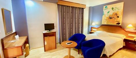 Una habitación de hotel con cama, escritorio, silla, televisor y un cuadro en la pared.