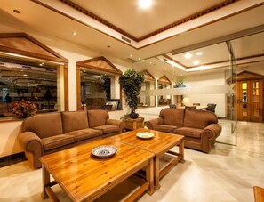 A spacious living area with a wooden coffee table, two brown sofas, and a large window. - Hotel Torrepalma (Alcala la Real)