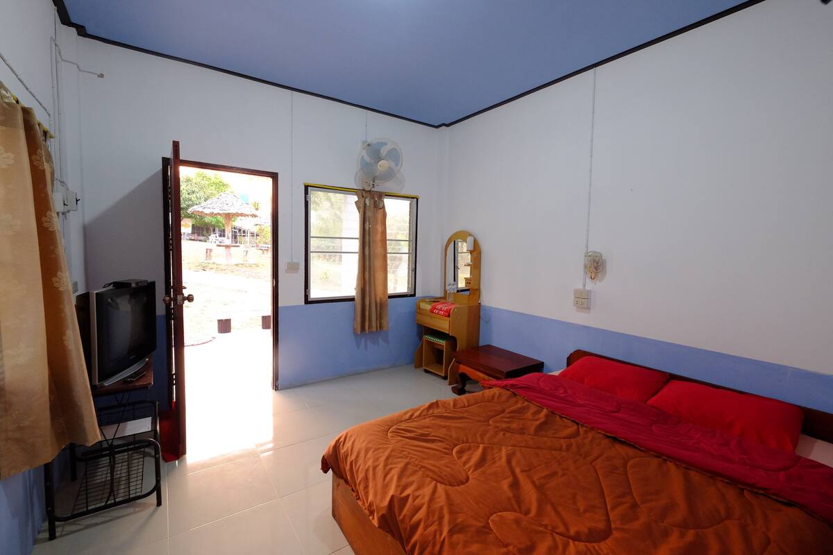 A bedroom with a bed, a TV, a desk, a mirror, and a window.