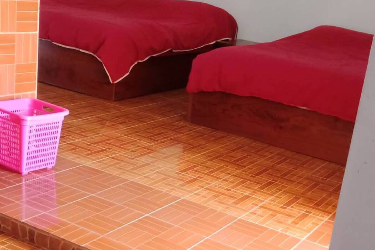 A room with a tiled floor, two beds with red bedding, a pink basket, and a wall-mounted light fixture.