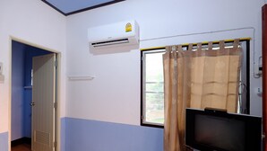 A room with a television on a stand, an air conditioning unit on the wall, a window with a curtain, and a door leading to another room.