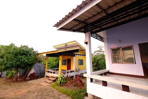 Uma casa de dois andares com fachada amarela e branca, varanda coberta e um jardim com plantas e uma estrutura de pedra.