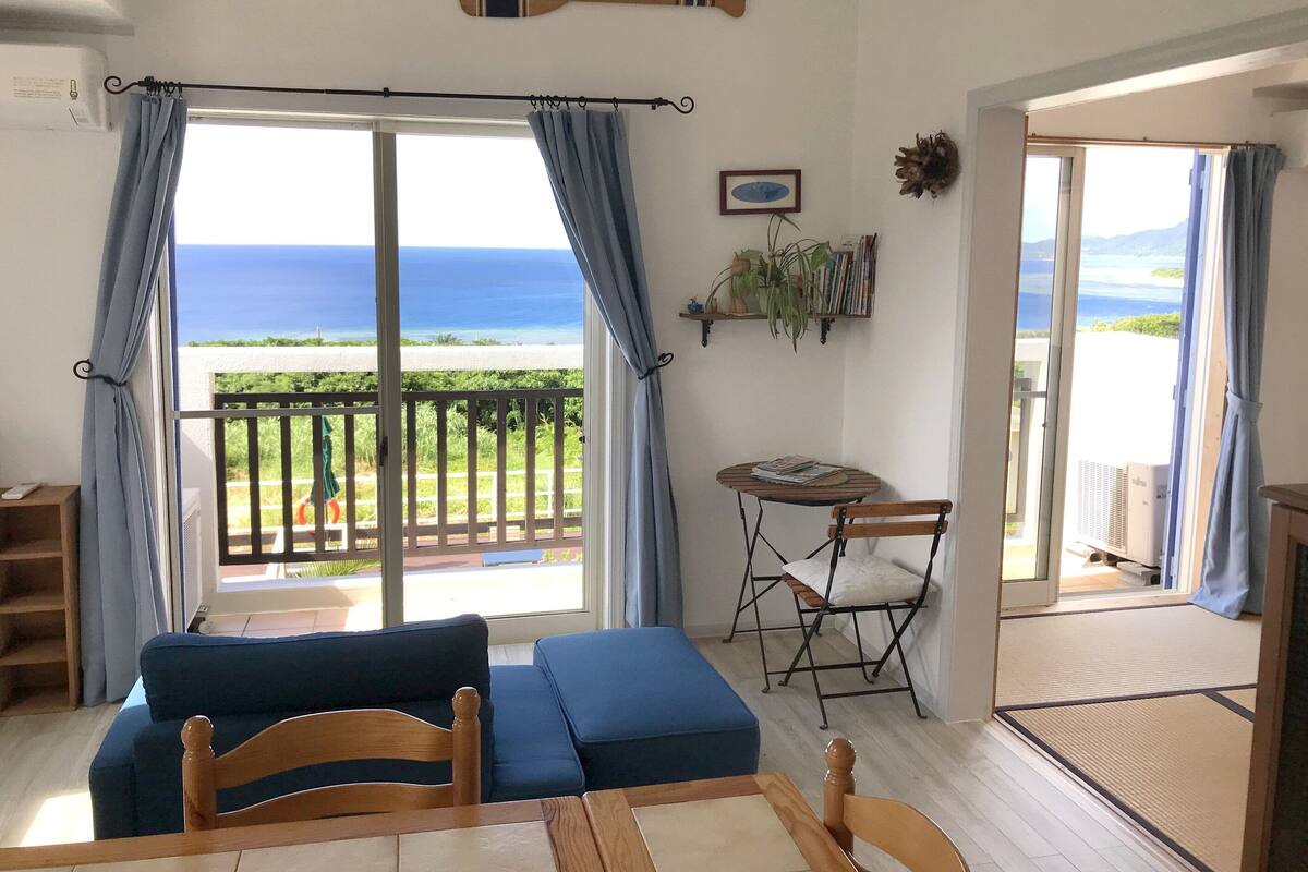 A room with a view of the ocean, a blue sofa, a wooden table, and a chair.
